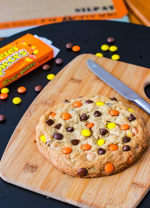 one giant peanut butter Reese's Pieces cookie on a wood board