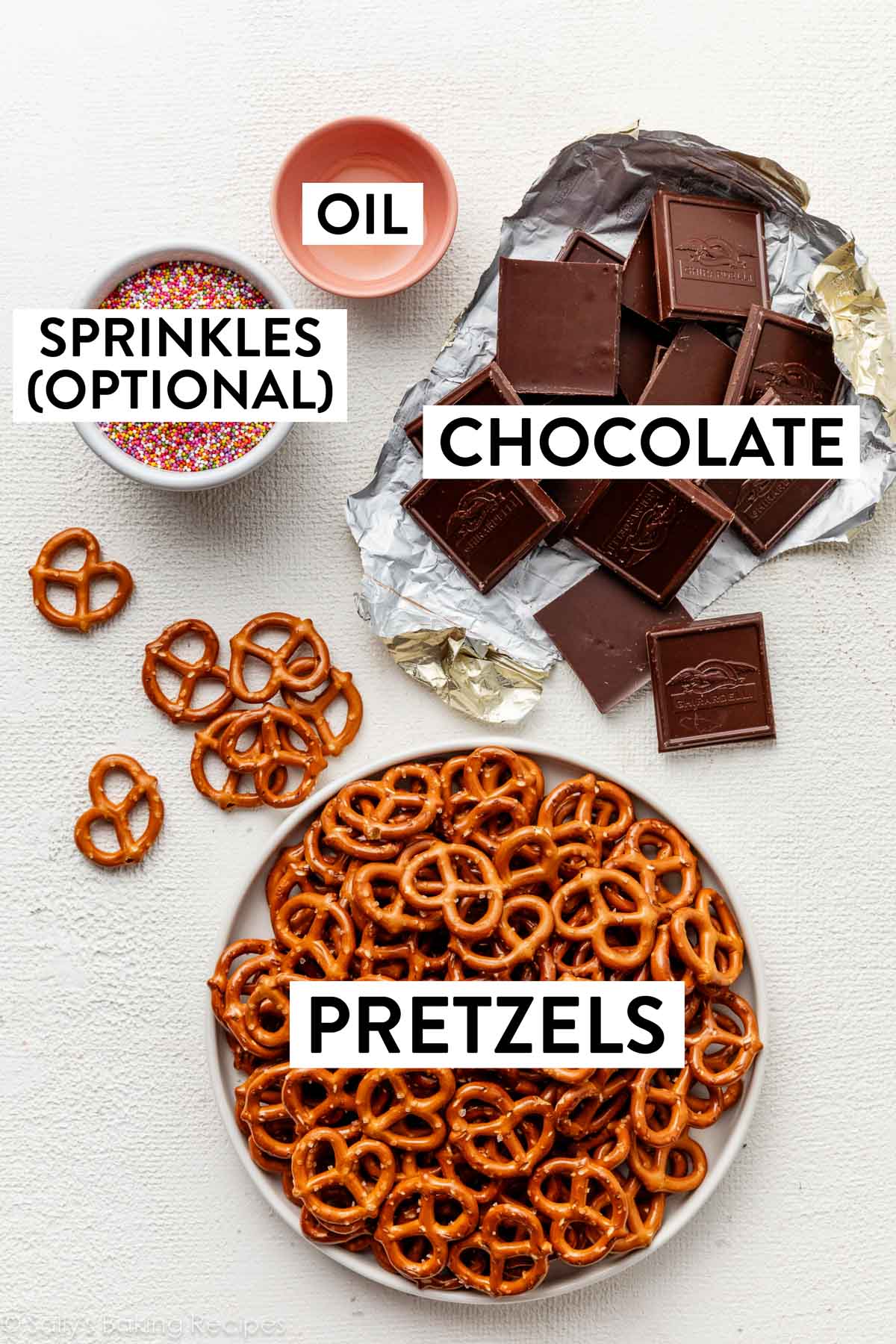 ingredients on white surface including chocolate, sprinkles, and small pink bowl of oil.