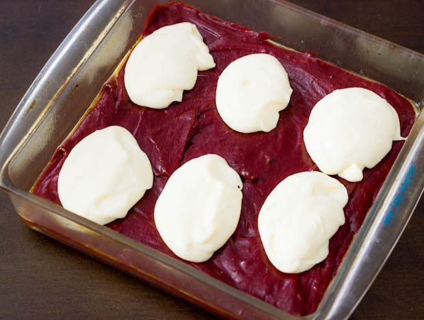 red velvet brownie batter with cheesecake mixture on top in a glass baking pan before swirling