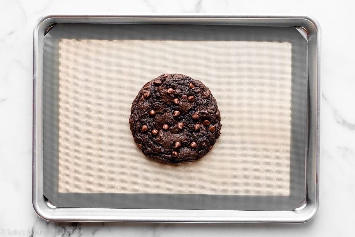 one giant double chocolate chip cookie in center of lined baking sheet.