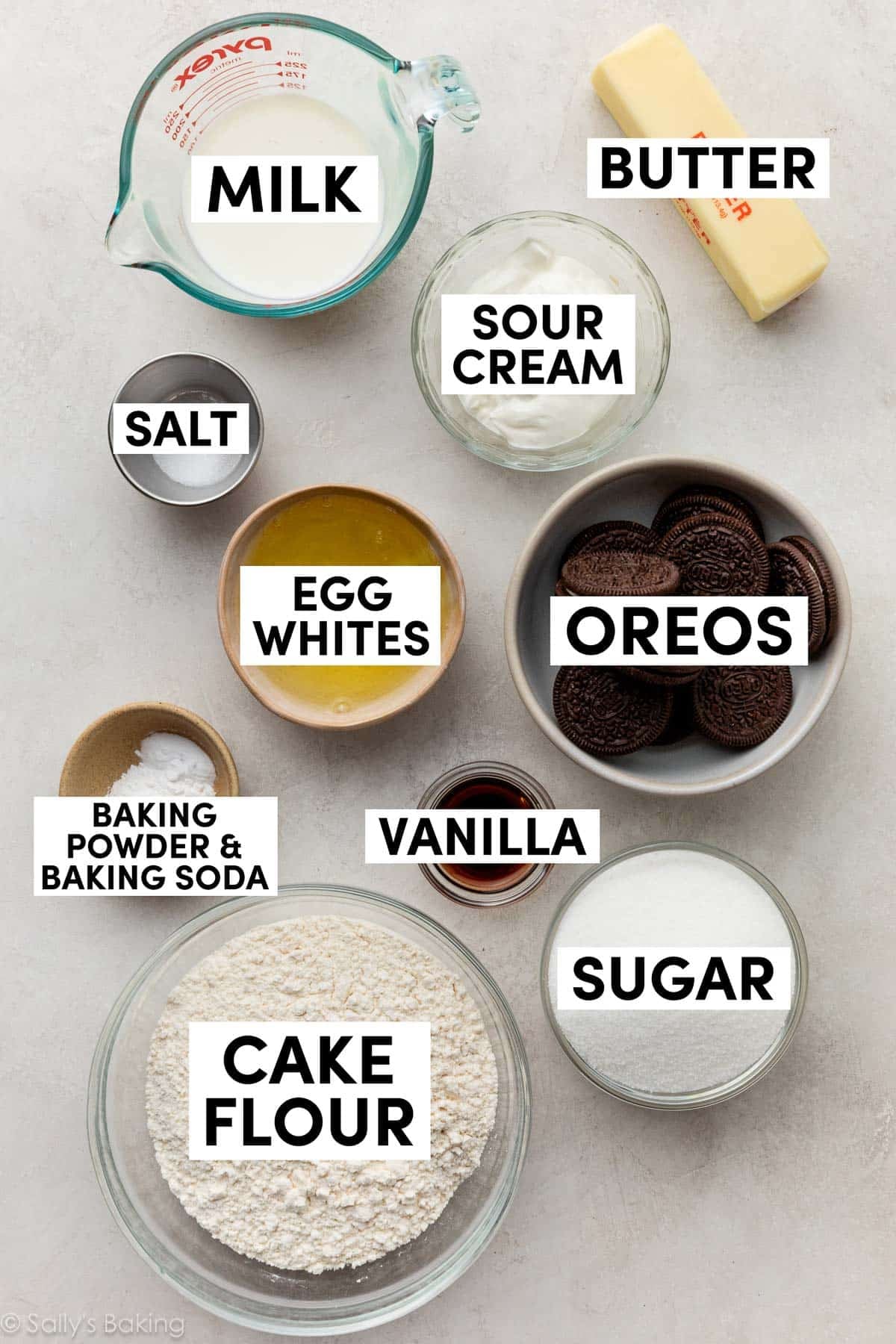 ingredients on gray surface including sour cream, butter, milk, egg whites, vanilla, sugar, and cake flour.