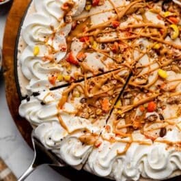 decorated peanut butter ice cream pie with Reese's Pieces, whipped cream, and peanut butter swirls on top.