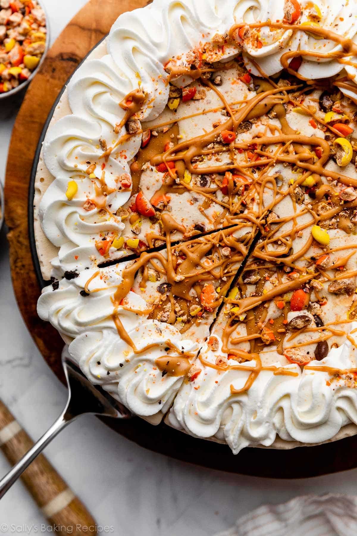decorated peanut butter ice cream pie with Reese's Pieces, whipped cream, and peanut butter swirls on top.
