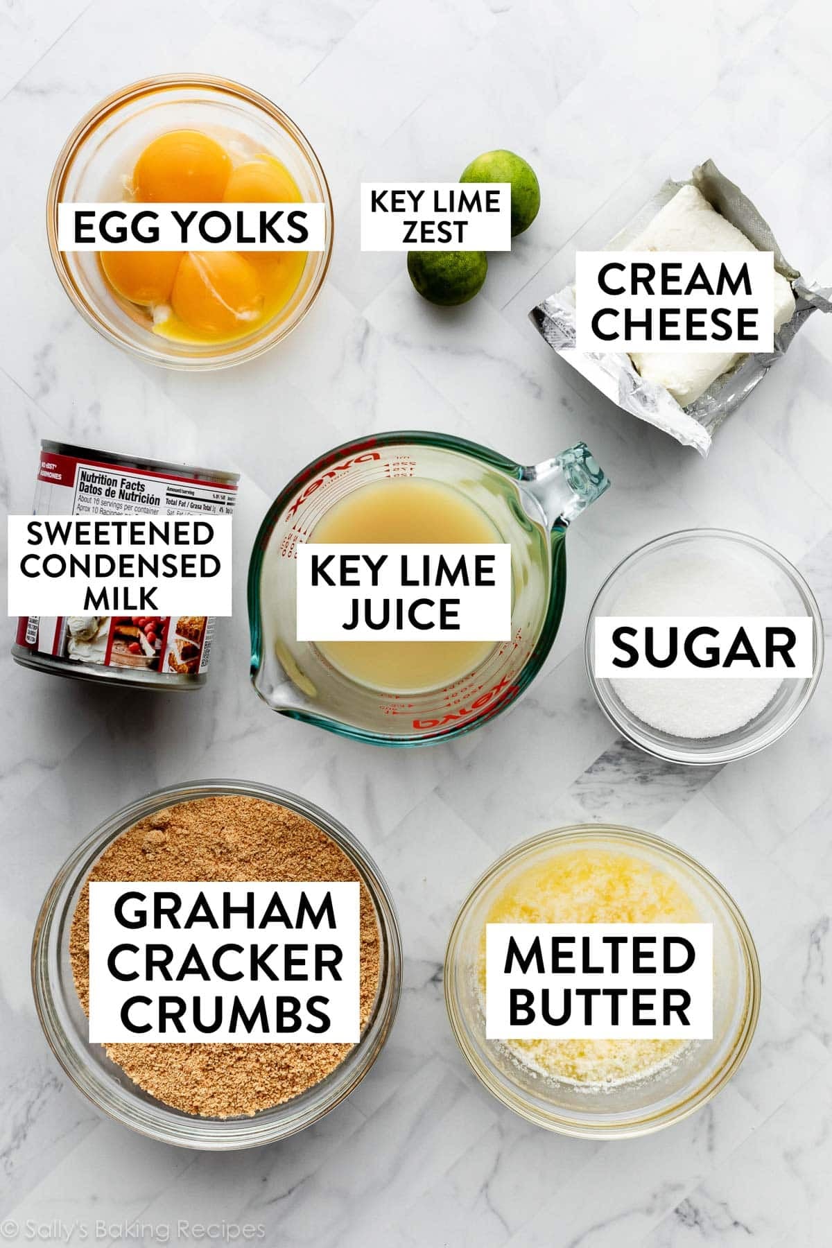ingredients on marble counter including cream cheese, sugar, key limes, melted butter, sweetened condensed milk, and egg yolks.