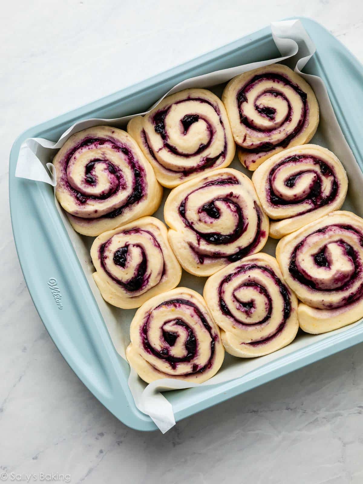 blueberry-filled cinnamon rolls before baking in blue square pan.