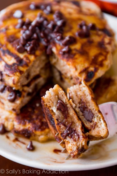 stack of whole wheat oatmeal chocolate chip pancakes with maple syrup on a white plate with a fork
