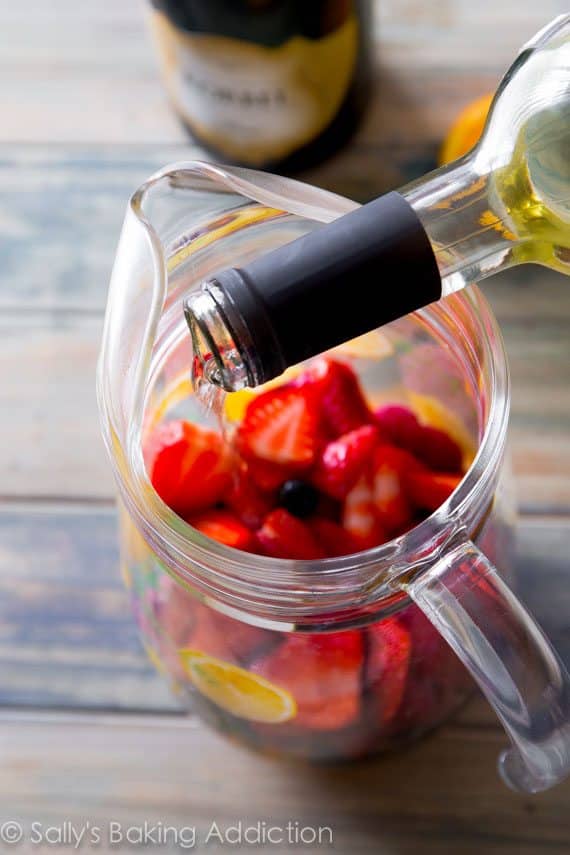 pouring white wine into a glass pitcher of sangria