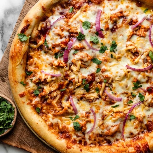 BBQ chicken pizza on wooden cutting board.