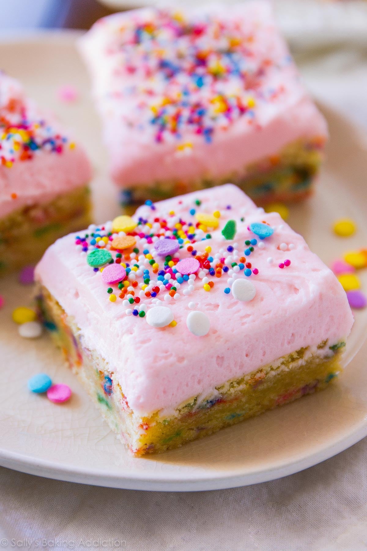 sugar cookie bars on a white plate with pink frosting and sprinkles