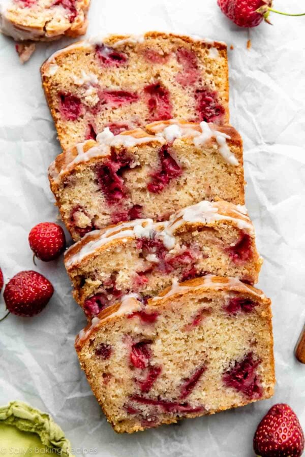 overhead photo of sliced and glazed strawberry bread on white parchment paper.