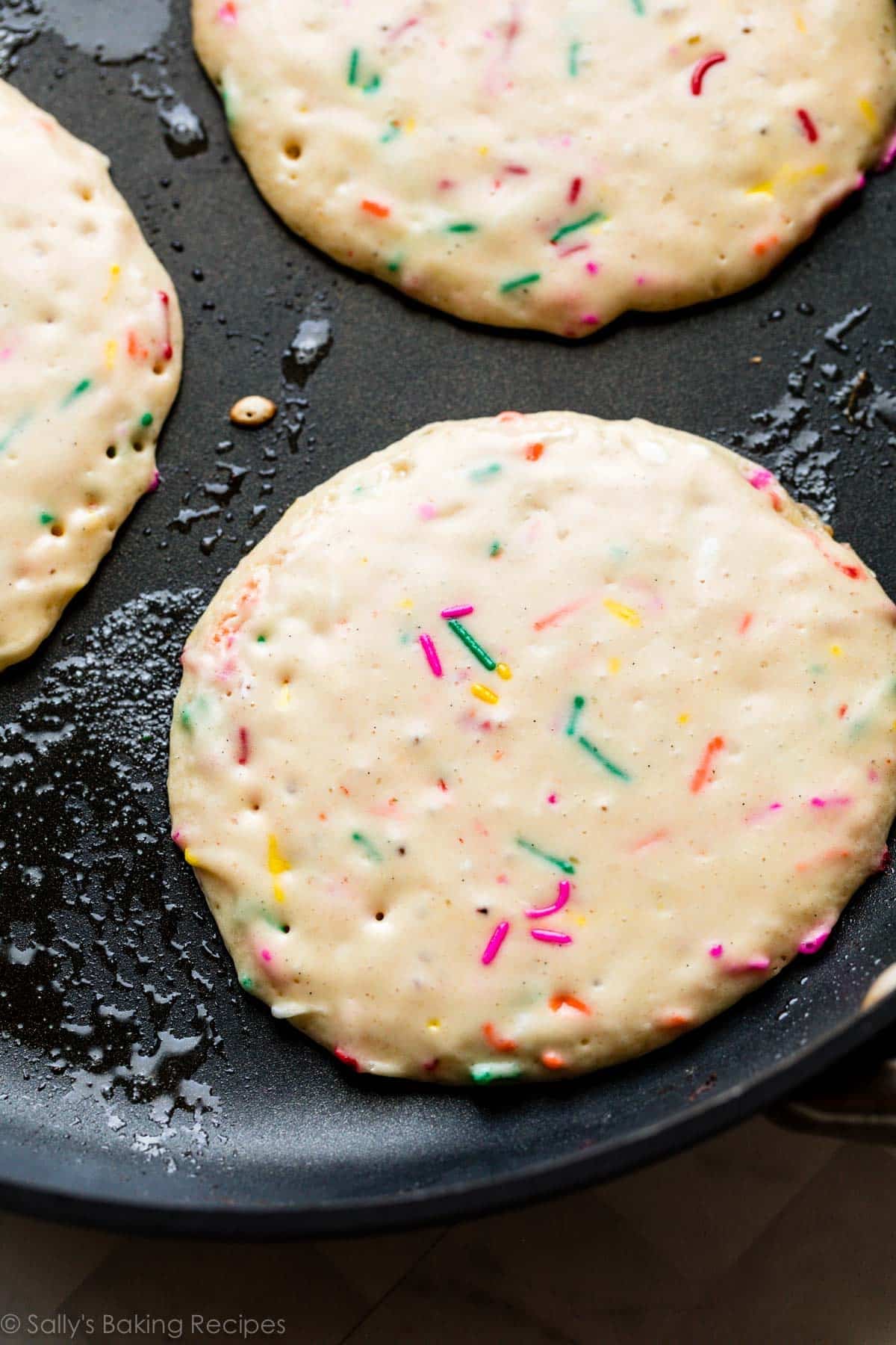 3 sprinkle pancakes cooking on a greased skillet.