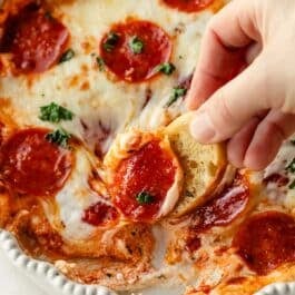 crostini being dipped in pizza dip with pepperonis on top.