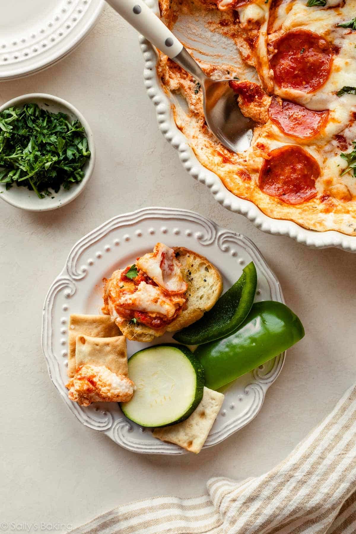 pizza dip on plate with dipping foods including sliced green pepper, zucchini, crostini, and crackers.