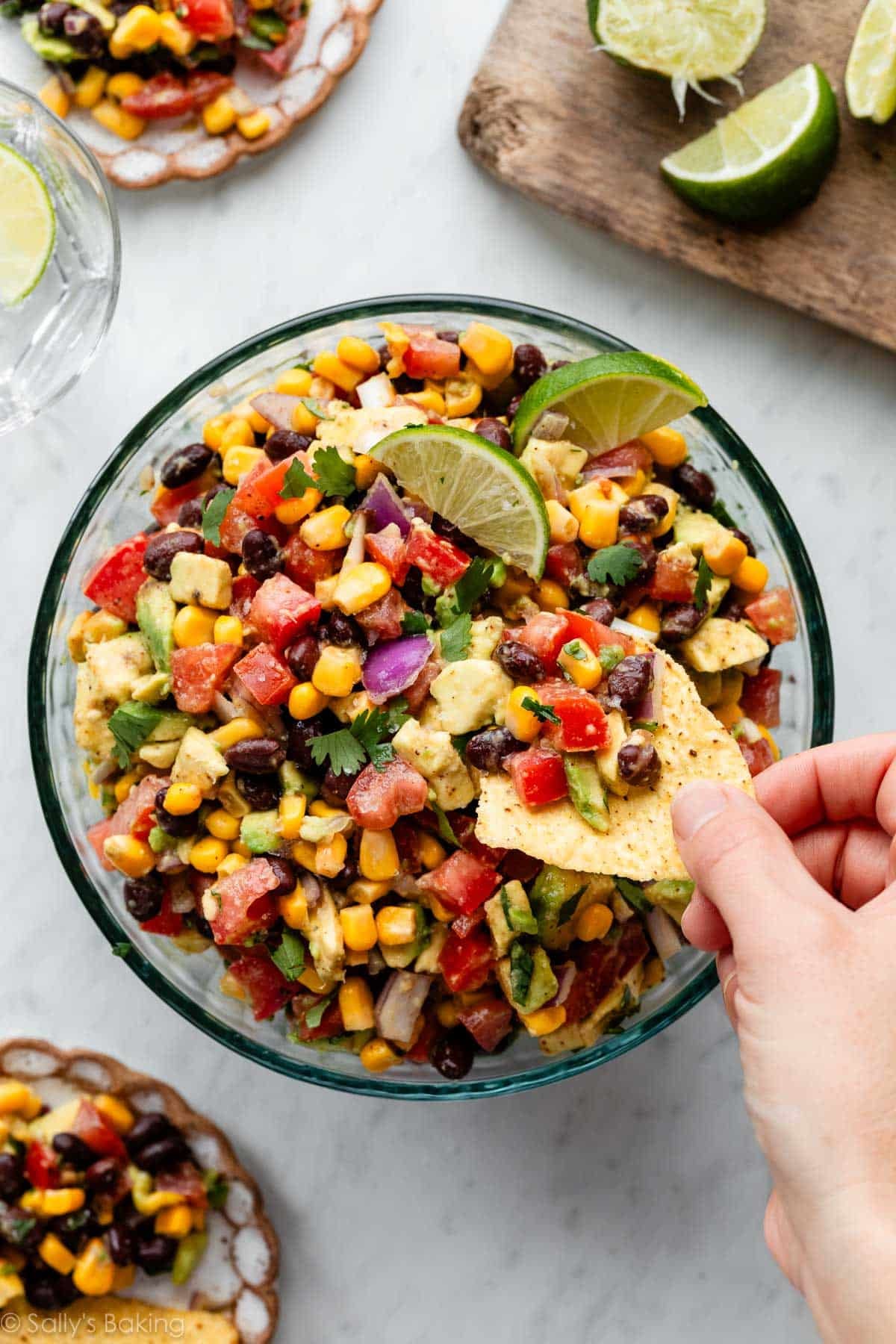 hand dipping a tortilla chip in black bean corn avocado salsa.