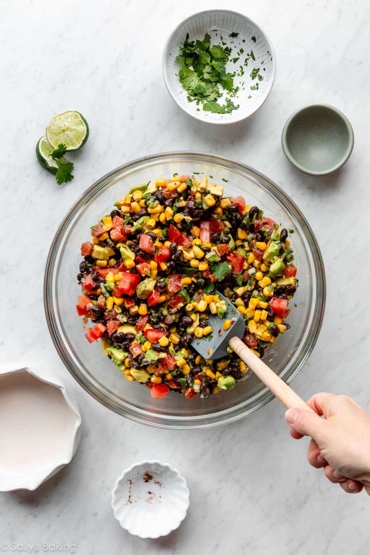 mixing fresh ingredients in a big glass bowl including corn, tomatoes, cilantro, and beans.