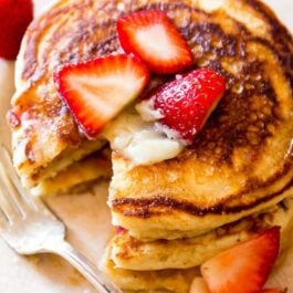 stack of strawberry buttermilk pancakes topped with honey butter and sliced strawberries on a white plate with a fork