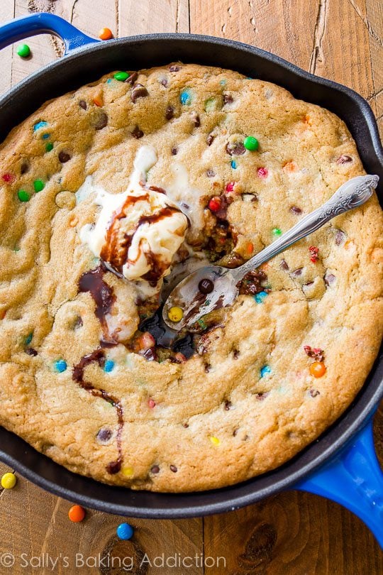 M&Ms chocolate chip skillet cookie topped with ice cream in a blue skillet with a spoon
