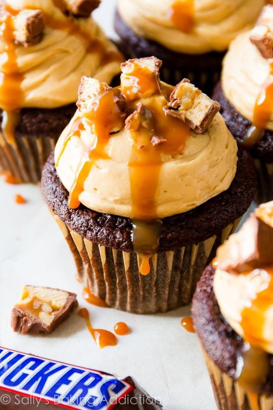 chocolate cupcakes topped with peanut butter frosting, chopped Snickers candy bars, and salted caramel