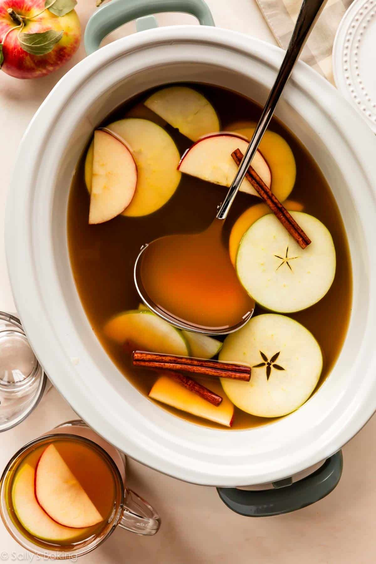 apple cider in slow cooker with cinnamon sticks and apples.