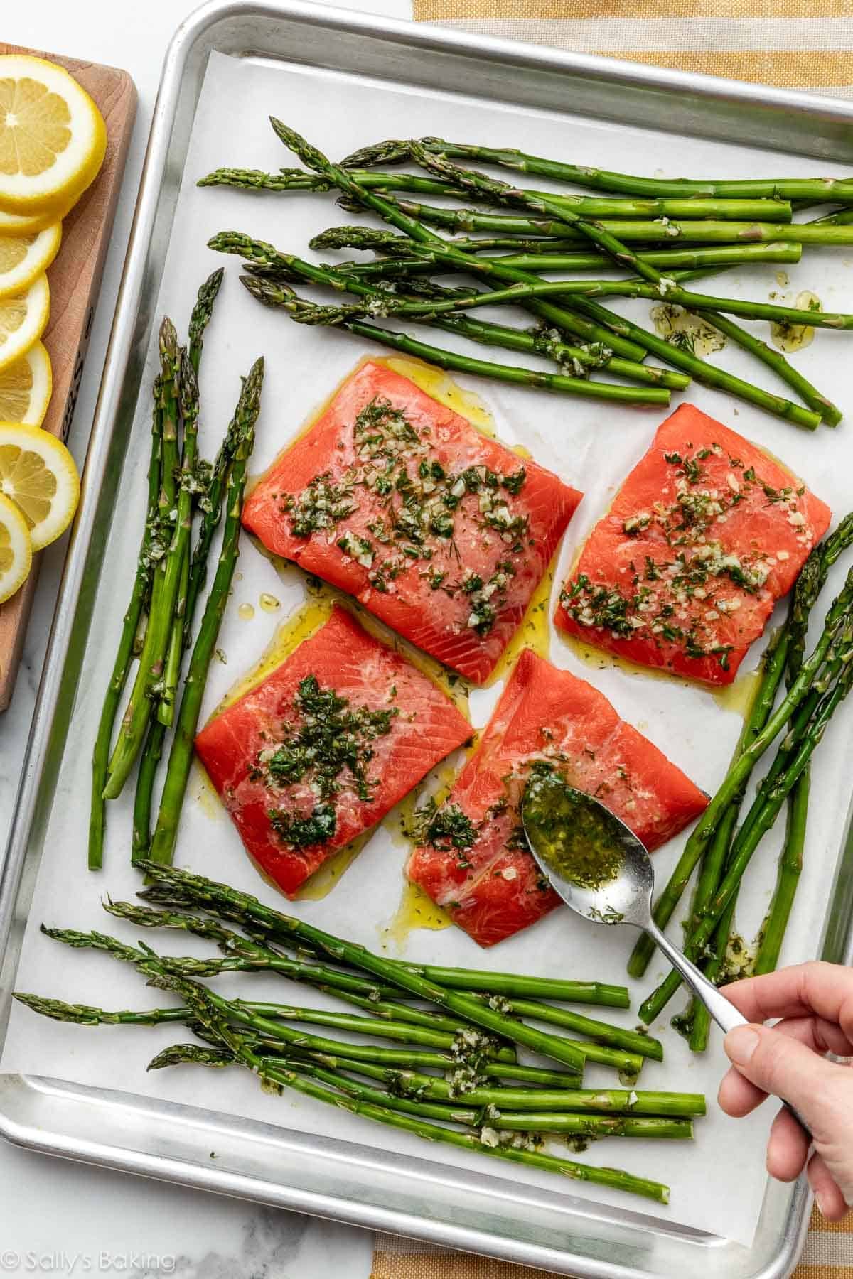 spooning sauce over salmon on sheet pan with asparagus.