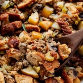 wooden spoon serving a spoonful of sausage herb apple Thanksgiving stuffing.