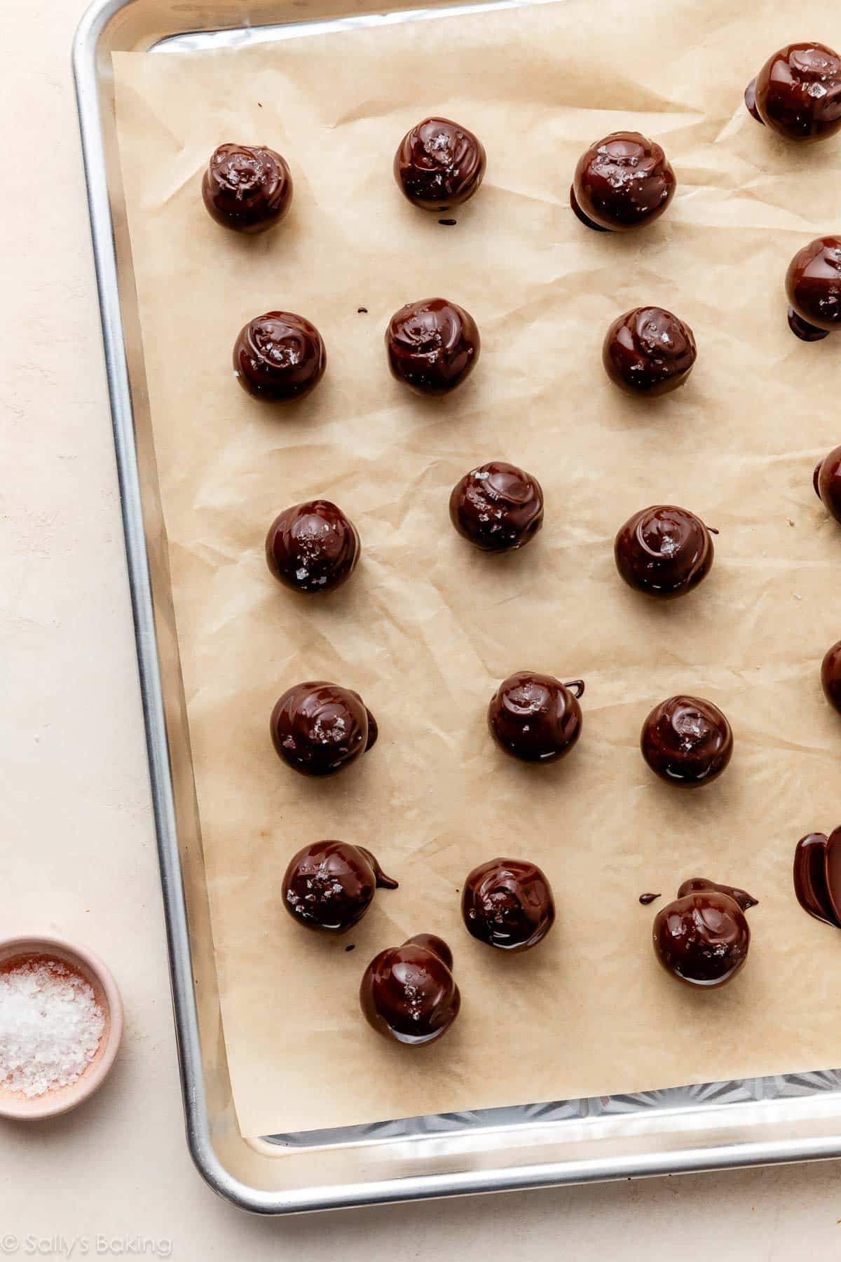 truffles coated in chocolate and topped with sea salt on linked baking sheet.