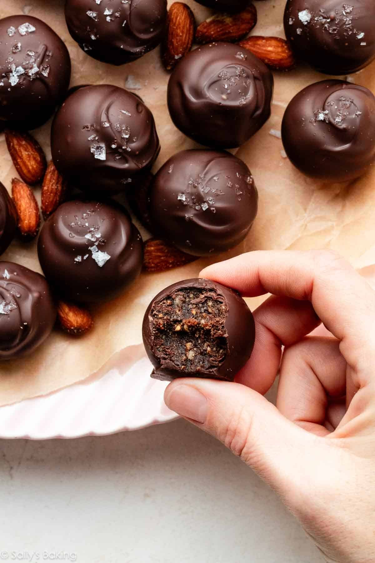 hand holding a bitten chocolate date and almond truffle.