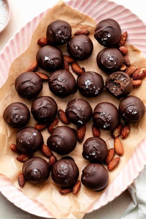 healthy date almond truffles coated in chocolate and sea salt placed with almonds on a pink plate.