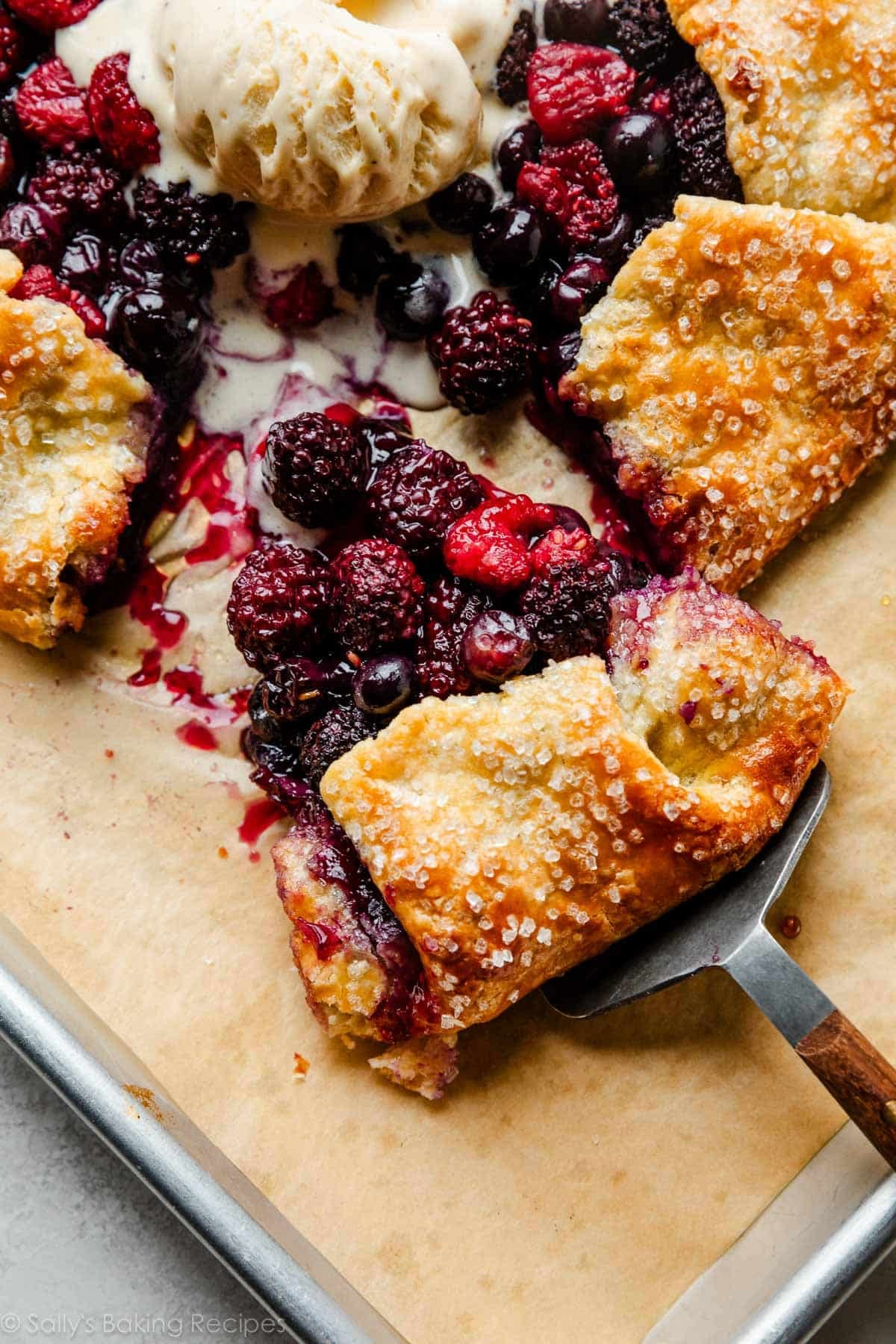 piece of mixed berry galette being removed from entire tart with pie server.