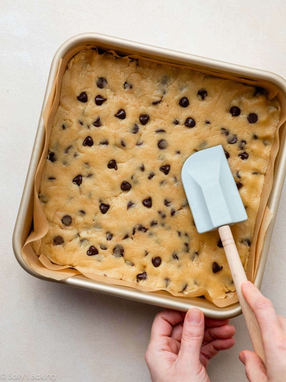spatula pressing dough into square baking pan.