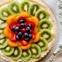 overhead image of fresh fruit tart with glass of sparkling water.