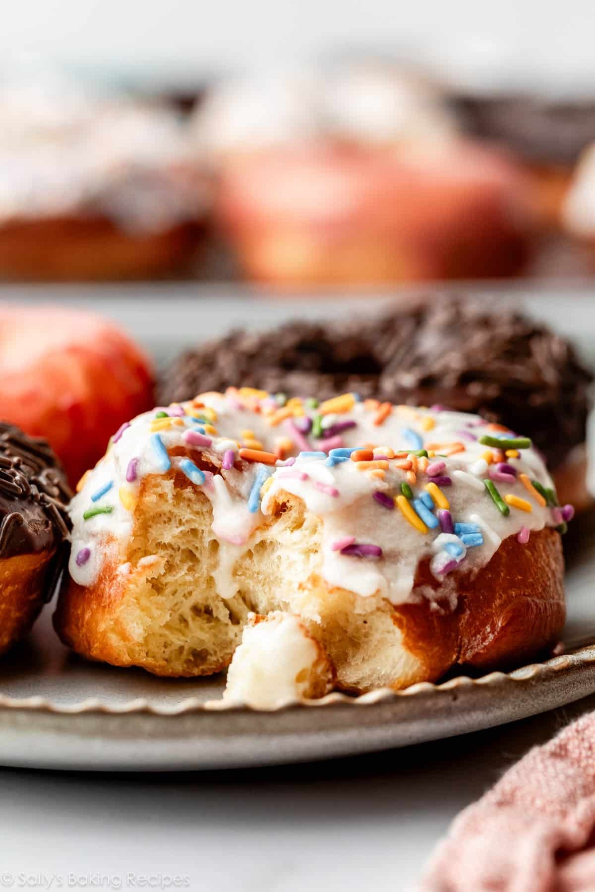 vanilla frosted doughnut with bite taken out on gray plate.