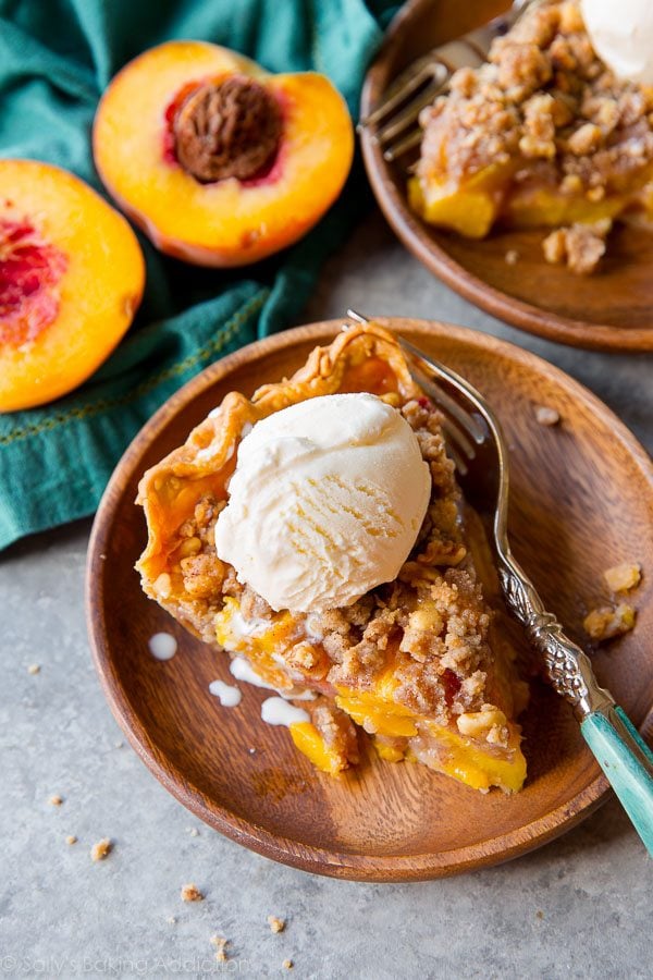 overhead image of a slice of peach crumble pie with a scoop of vanilla ice cream on a wood plate with a fork