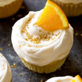 mimosa cupcakes topped with champagne frosting, an orange slice, and gold sprinkles