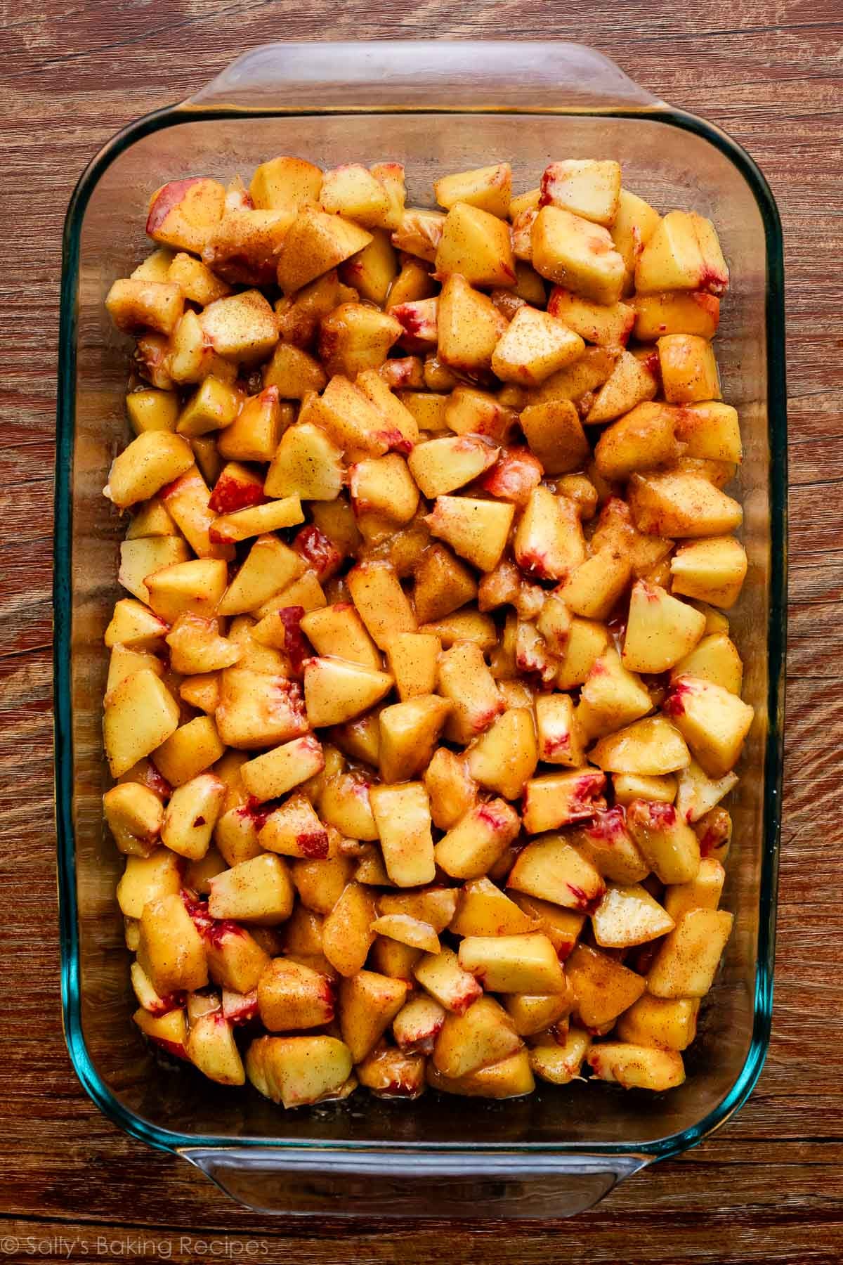 wet peaches filling in glass baking pan on wooden backdrop.