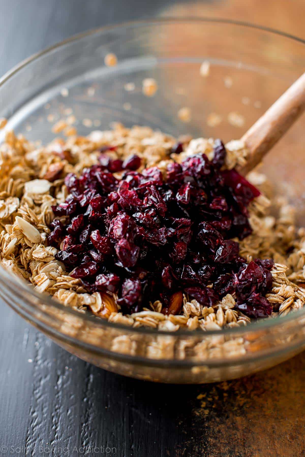 dry ingredients and dried cranberries in a glass bowl with a wood spoon