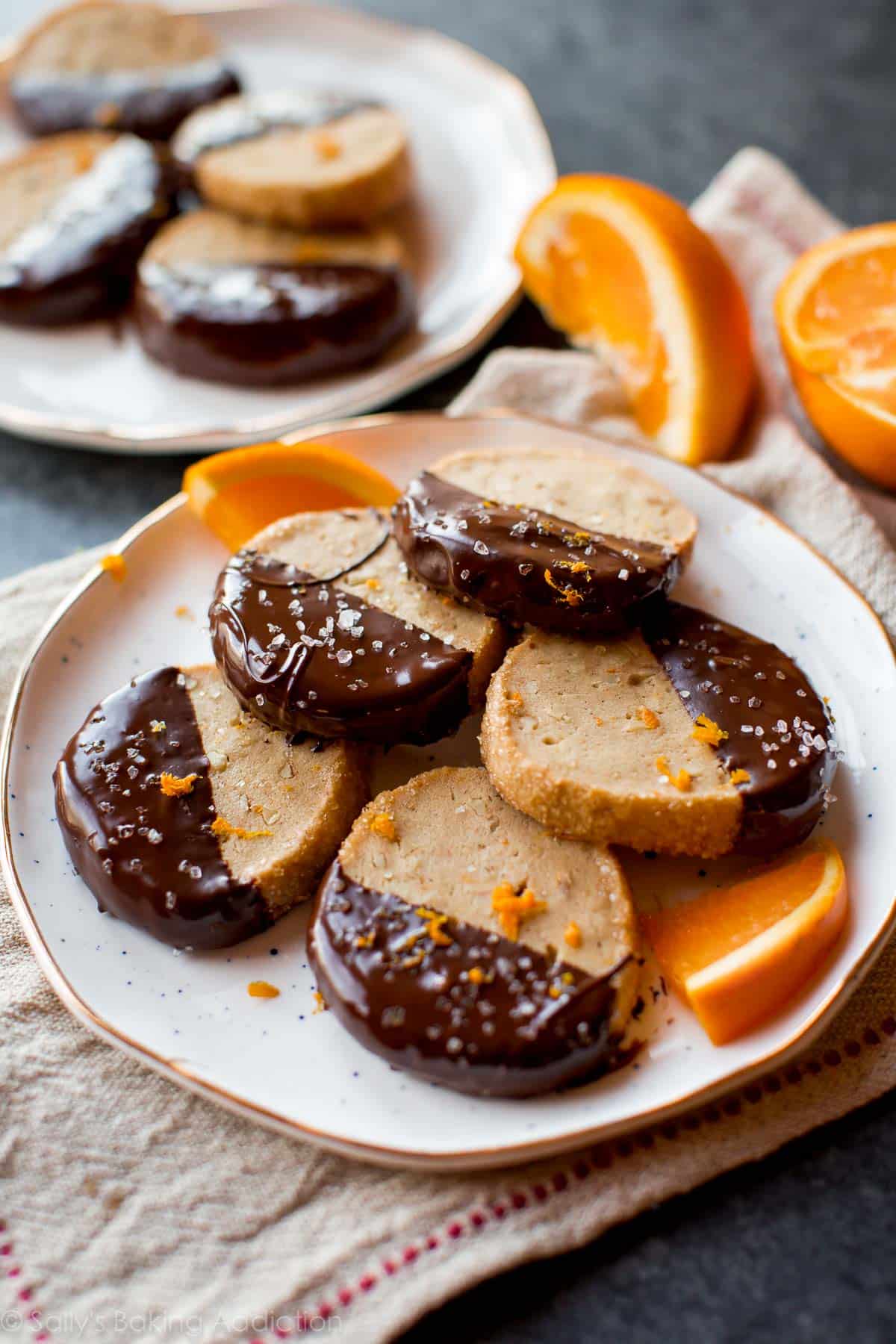 orange slice and bake cookies with half of each cookie dipped in dark chocolate on a white plate