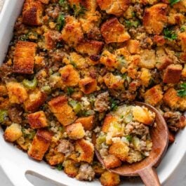 wooden spoon scooping out cornbread stuffing from white dish.