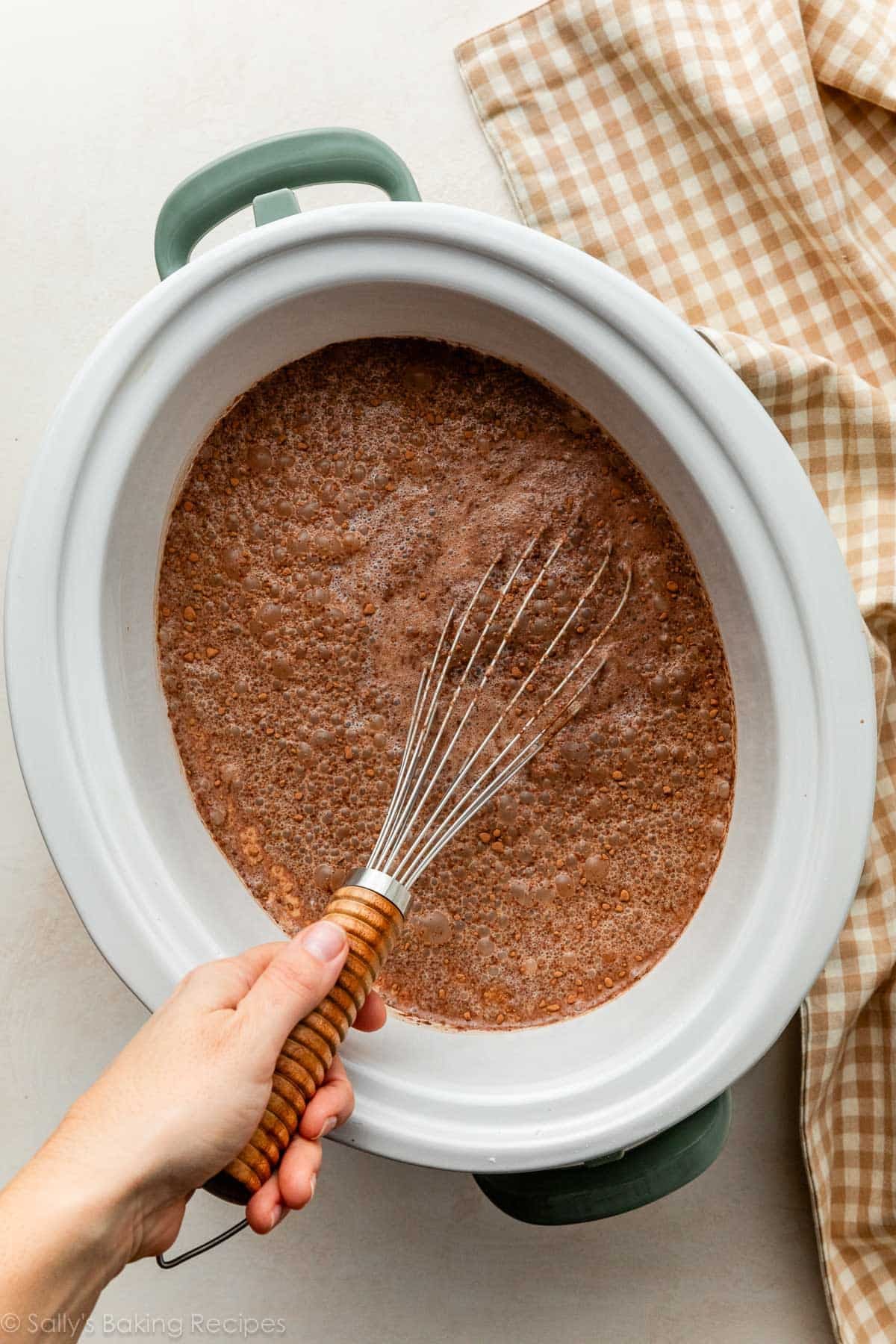 whisk mixing cocoa ingredients in slow cooker with blue handles.