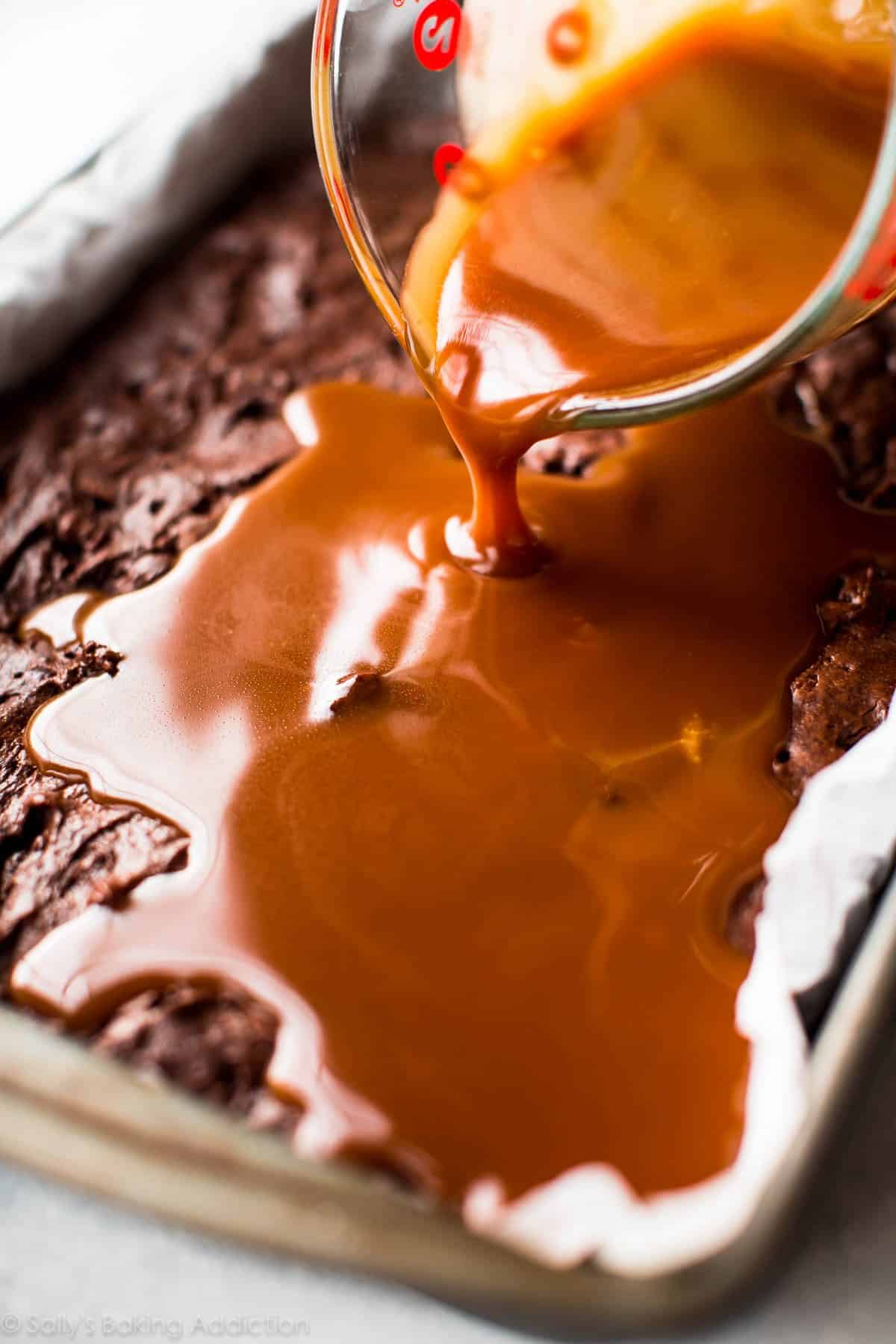 pouring salted caramel sauce onto brownies in a baking pan