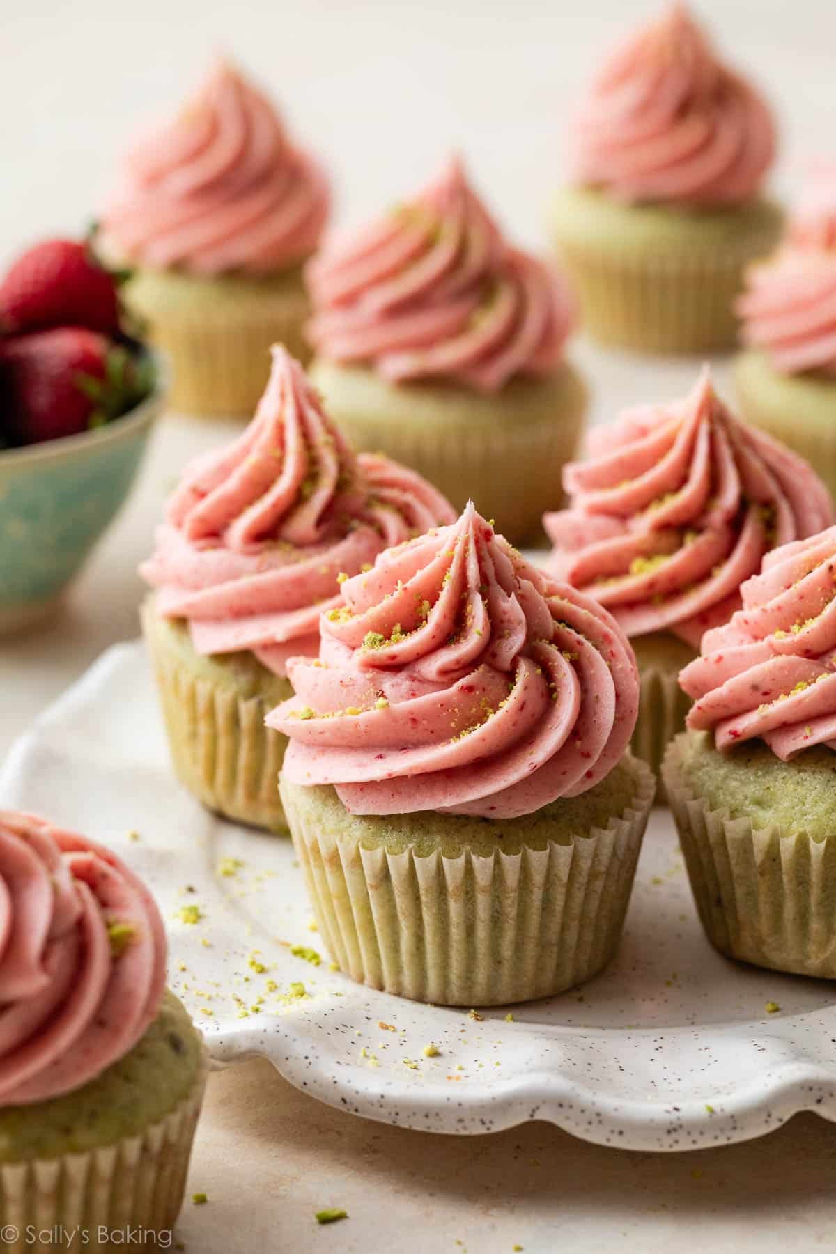 pistachio cupcakes with pink strawberry buttercream frosting on top on a white plate.