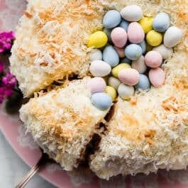 Easter cake decorated like a nest with a Bundt cake, coconut, and Easter chocolate egg candies on pink serving dish.