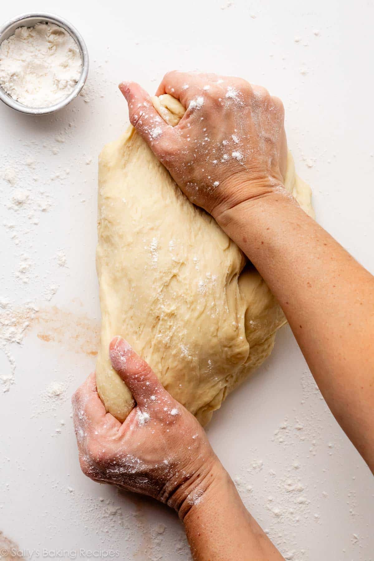 floured hands stretching dough on white surface.