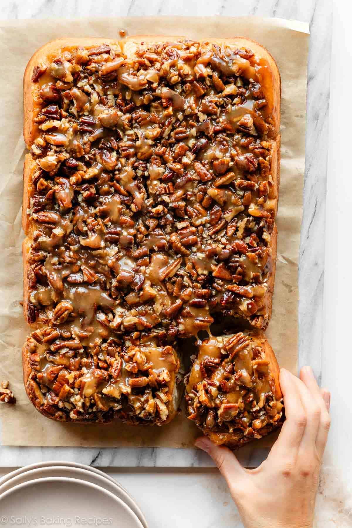 hand pulling a maple pecan sticky bun away from the batch.