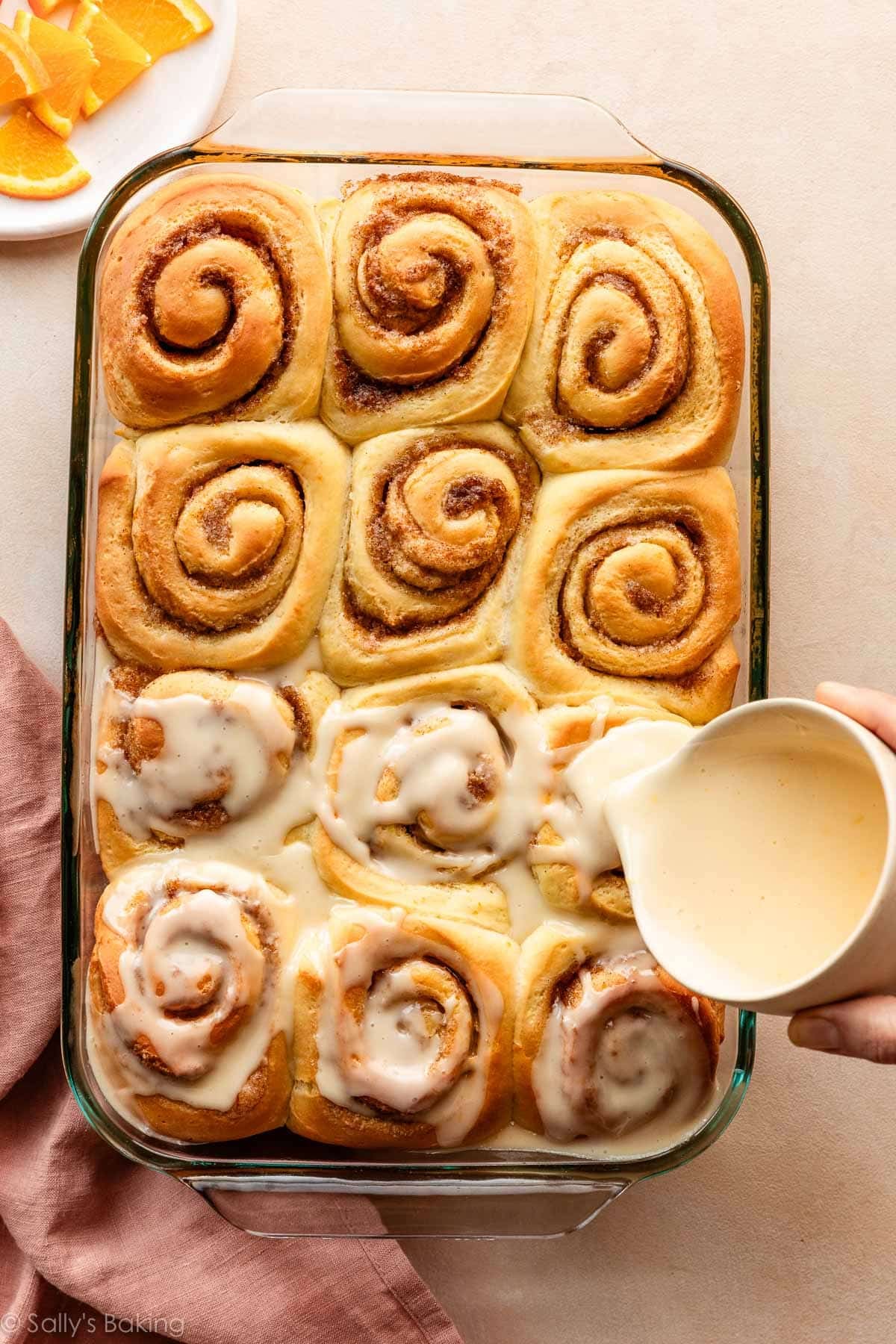pouring orange icing on orange sweet rolls.
