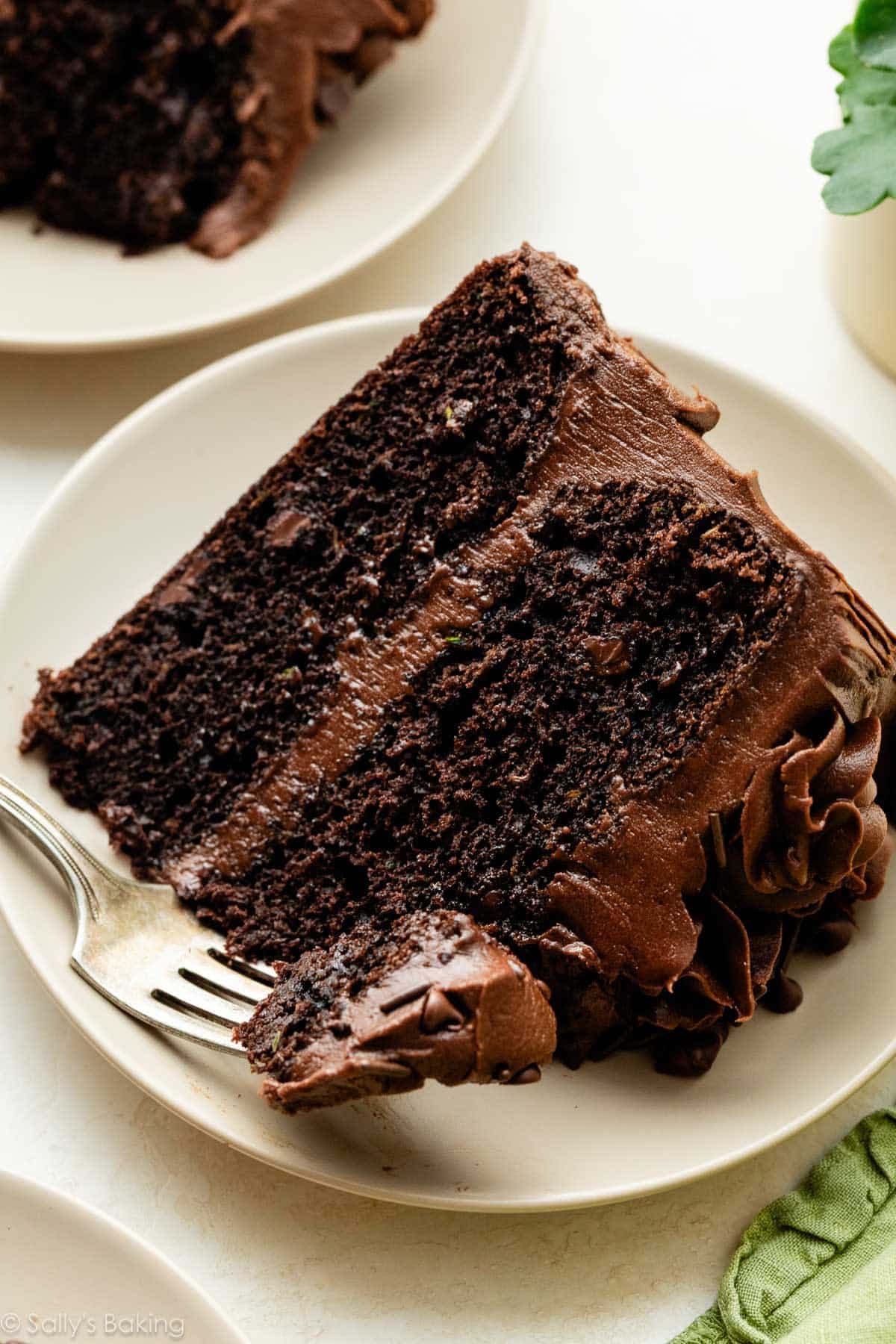 slice of chocolate zucchini cake with chocolate frosting on beige plate.