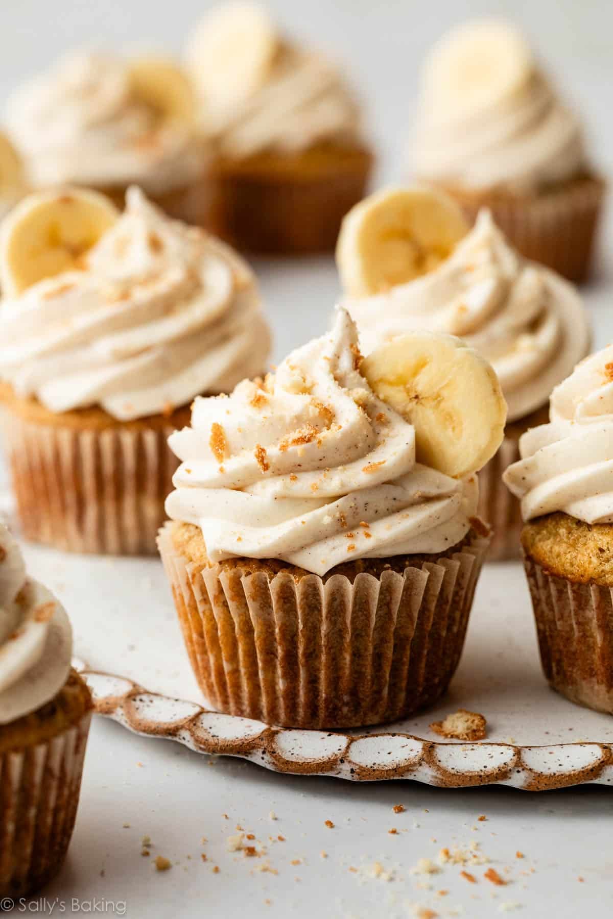 banana cupcakes with cinnamon cream cheese frosting, banana slice, and crushed nilla wafers on top.