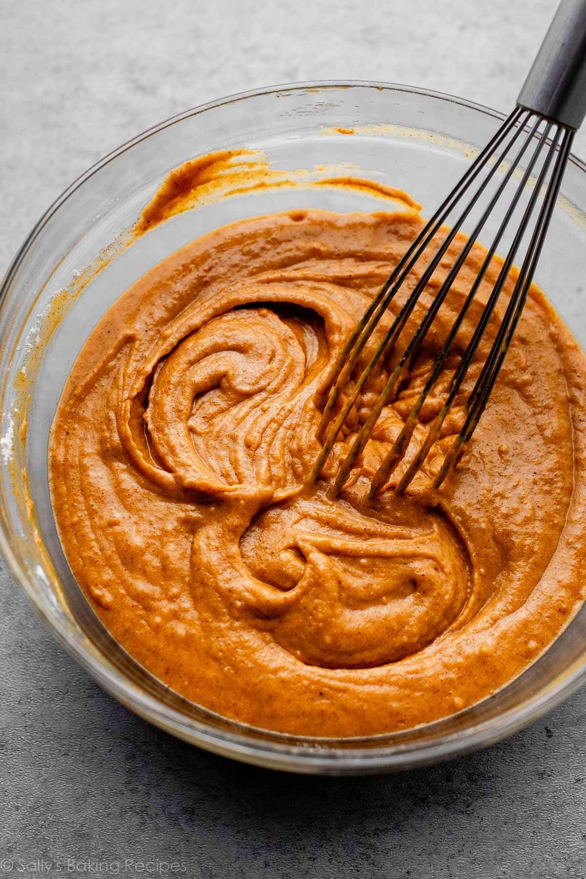 orange batter in glass bowl with whisk.
