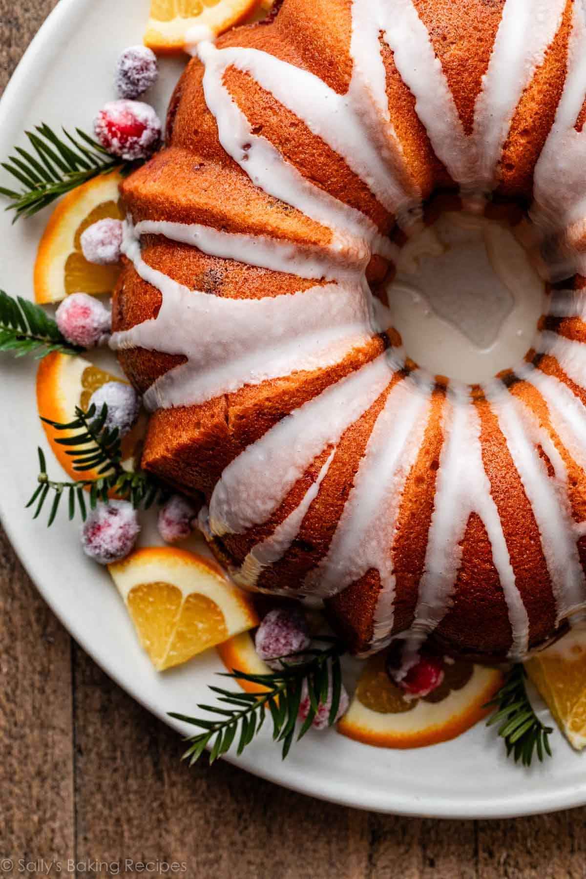 glazed orange Bundt cake on platter with orange slices and fresh pines.