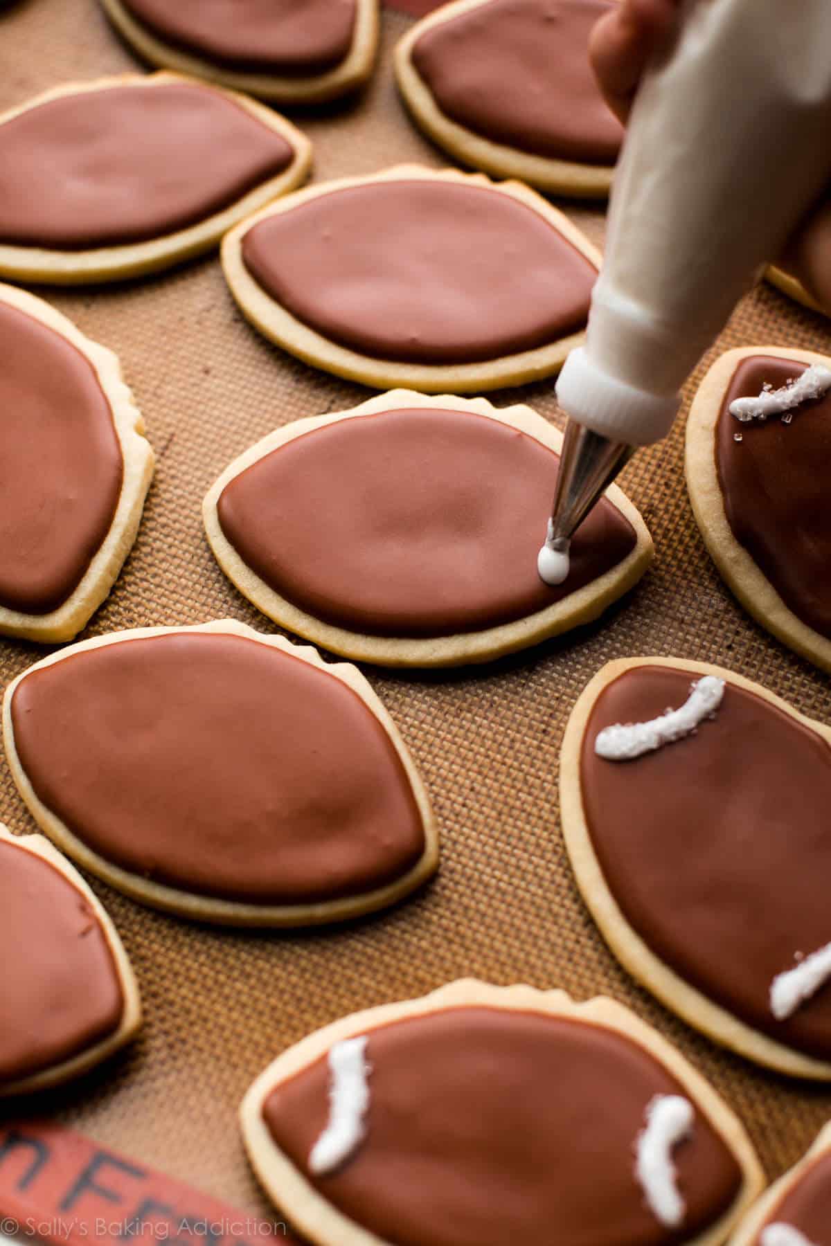 piping white details onto football sugar cookies